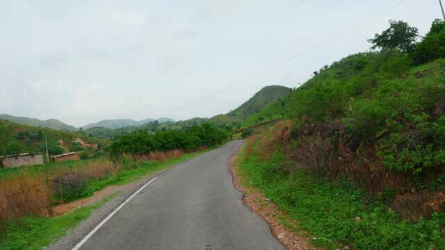 4K POV shot of Driving on empty road at Rayta hills in Sahyadri range at Udaipur, Rajasthan, India. Driving on green hills during moody monsoon day. Road trip, travel and adventure concept