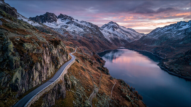 Mountain landscape with winding road and lake at sunset in the Alps creating a scenic view of nature's beauty and changing colors