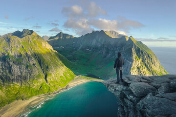 Person standing on rocky cliff overlooking fjord and mountains in Norway
