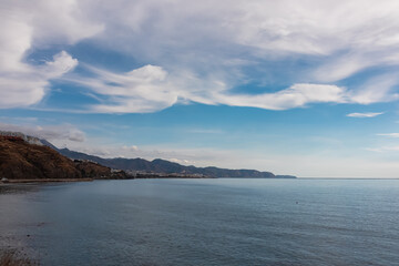 Panoramic view of the vast Mediterranean Sea stretching towards the horizon, bordered by the rugged cliffs of Torrox Costa under dramatic cloudy atmosphere on a peaceful afternoon in Andalusia, Spain