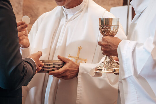 Detalle de las manos de dos sacerdotes cat&oacute;licos, uno sostiene un c&aacute;liz y el otro una hostia consagrada. Concepto de comuni&oacute;n y eucarist&iacute;a.