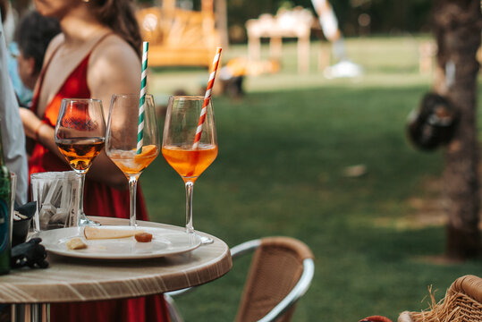 Dos copas con c&oacute;cteles y pajitas de colores sobre una mesa alta de terraza con fondo de jard&iacute;n. Concepto de verano, social y aperitivo.
