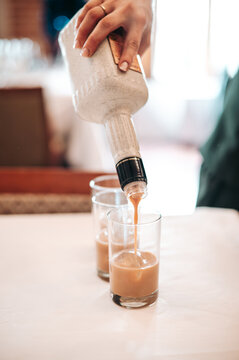 Detalle de una mano vertiendo licor marr&oacute;n en un vaso de chupito desde una botella blanca. Concepto de bebida alcoh&oacute;lica y cocteler&iacute;a.