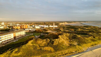 Drone aerial panorama of Berck-sur-Mer, France, showing striped lighthouse, seaside town and coastal dunes with sandy beach, seawall and bay under warm evening light