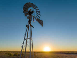 Metal Windmill In Grassy Field with Orange and Blue Sunset Sky