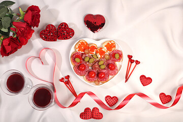 Heart of fresh canapes with salami, caviar, cheese and grapes for a buffet with roses, red wine and red hearts on the festive table. Valentine's Day dishes, advertising banner, bar invitations, menu