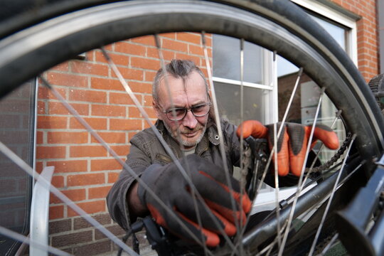 Man repairing bicycle near brick building during the daytime for transportation
