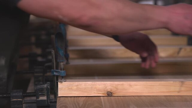 Detailed View Of Hands Fastening Clamp Onto Neatly Arranged Wooden Planks In Workshop Setting. Media
