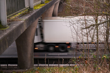 A heavy transport truck drives along a highway under a bridge, representing the essential vehicle traffic by motion blur and equipment used in the modern transportation industry