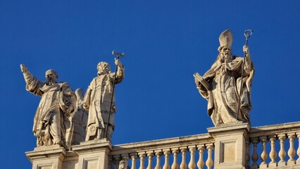 Rome, Italy - 14 January 2025. Religious statues with distinct items like a cross and staff stand on San Giovanni in Laterano&rsquo;s rooftop, framed by balustrades and clear sky.
