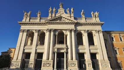 Rome, Italy - 14 January 2025. The Basilica of San Giovanni in Laterano displays its symmetrical facade with arches, columns, and rooftop saint statues lit by afternoon sun.