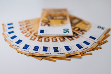 Stacks of fifty euro banknotes arranged in a circular pattern on a clean white surface, showcasing the intricate designs and vibrant colors of currency notes