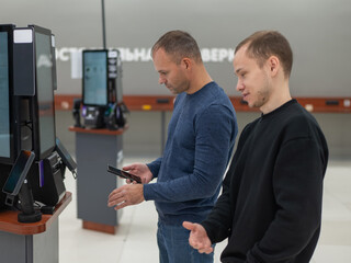 Two Caucasian men use a self-checkout machine at a hardware store.
