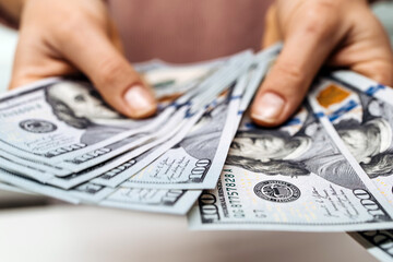 Hands holding multiple hundred-dollar bills, showcasing the concept of wealth and financial...