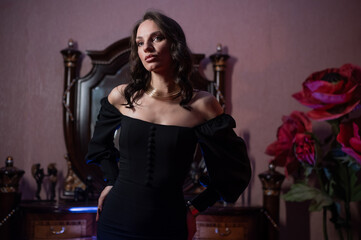 A beautiful brunette in a black evening dress poses in front of a retro-style mirror. 