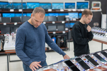 Two Caucasian men are choosing a smartphone in a store.