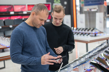 Two Caucasian men are choosing a smartphone in a store.