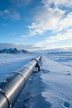 A pristine winter landscape is bisected by a straight pipeline, with the endless snow-covered terrain.