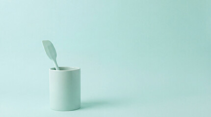Minimalist Studio Shot of a Ceramic Cup with a Spoon on a Solid Light Teal Background with Copy Space