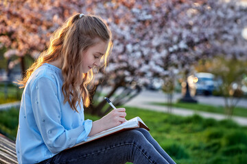 young female student taking notes in the park