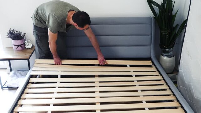 Self-assembly using a guide. House design. Close-up of a man's hands assembling a wooden bed using a screwdriver to insert screws into the bed frame.Collection of wooden furniture. Husband for an hour