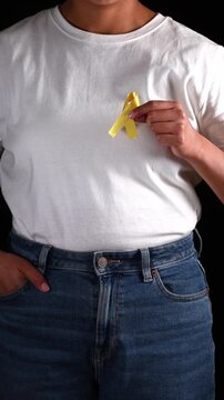 Close-up of an anonymous woman holding a yellow ribbon in her hand and placing it on her chest. Awareness campaign for bladder cancer, sarcoma, and bone cancer