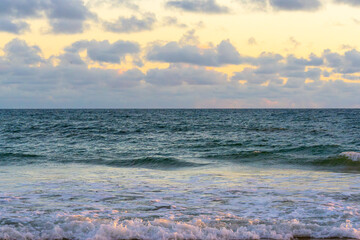 Gentle waves roll onto the shore beneath a softly colored sunset sky.