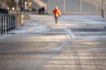 People walk on frosty asphalt pavement on city sidewalk covered with technical salt in cold winter...