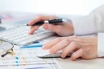 A woman working on an accounting report with a computer. Close-up of her hands.