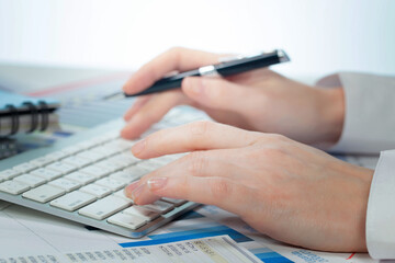 A woman working on an accounting report with a computer. Close-up of her hands.