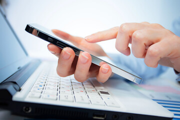 A woman works with a smartphone in the office, on a report. Close-up of her hands. 	