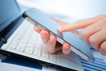 A woman works with a smartphone in the office, on a report. Close-up of her hands. 	