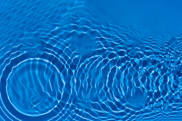 Blue water with ripples on the surface. Defocus blurred transparent blue colored clear calm water surface texture with splashes and bubbles. Water waves with shining pattern texture background.