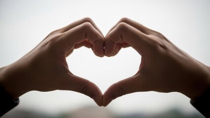 Obraz premium Hands forming heart shape silhouette against bright overcast sky