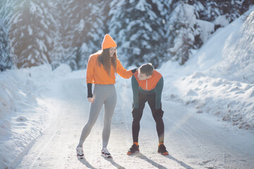 Young active couple resting after a winter run, standing together in a snowy landscape and catching their breath