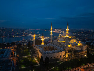 Naklejka premium Illuminated Letters Between Minarets (Mahya), Ramadan Background in the Istanbul Streets, Welcome Ramadan Month Text, Ramadan Kareem Drone Photo, New Valide Mosque Uskudar, Istanbul Türkiye (Turkey)