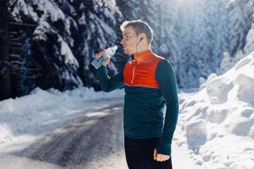 Male runner drinking water before a winter run in the snow