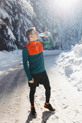 Male runner drinking water before a winter run in the snow