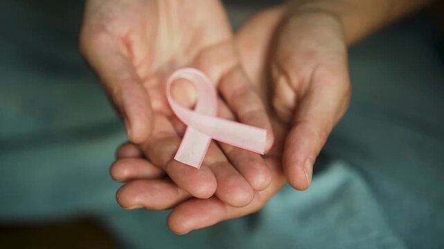 Detailed shot of pink awareness ribbon resting on woman's open hands, representing medical support and solidarity during October awareness month.