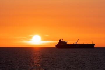Silhouette of a fuel tanker ship sailing on the horizon of the Baltic Sea near Estonia during a vibrant orange sunset