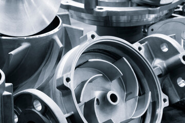 A collection of metal parts manufactured on a modern programmable metalworking CNC machine lie on the machine's metal work table, industrial metalworking concept background.