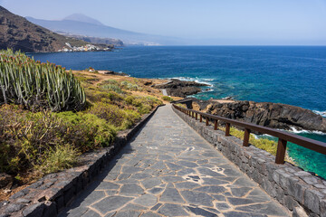 Stone pathway with wooden railings descending coastal cliffs toward turquoise ocean cove and Mount...