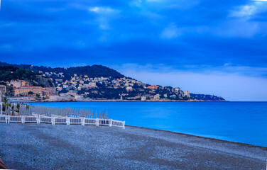 Striped umbrellas on a pebbled beach under dark sunset clouds in Nice, France