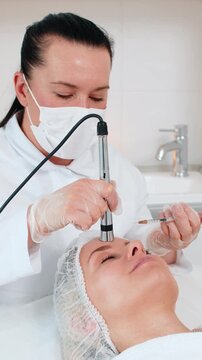 Injection-free mesotherapy or electroporation. Beautician doctor makes client adult woman forehead face therapy in beauty clinic salon. Girl skin care anti-age spa procedure. Aesthetic cosmetology.