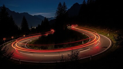 Nighttime highway curves with car light trails through mountain landscape.