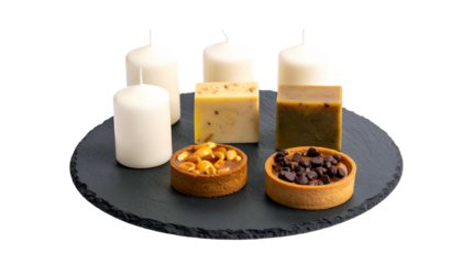 Composition of candles, soap, and tarts on a dark circular slate against black