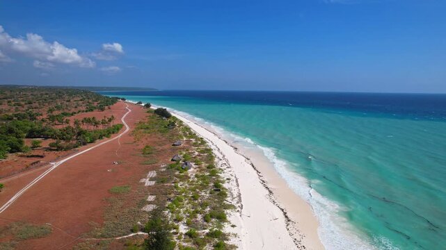 Aerial drone diving footage in a white sandy beach of Sabu island, Indonesia, with turquoise coastline, blue ocean sea, and redish grasses coastline, in a blue sky atmosphere