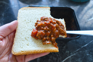 Bolognese on bread. Hand holding sliced bread topping with Bolognese.