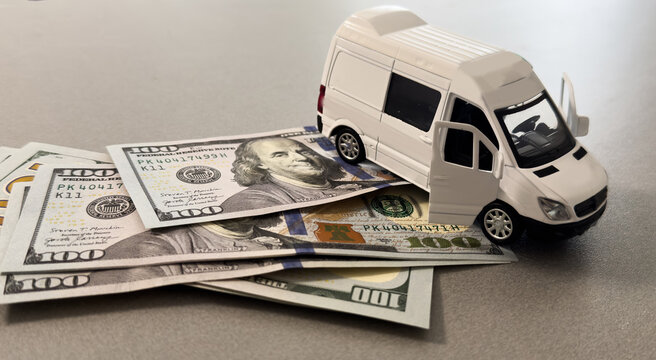  Miniature van on stack of dollar bills, symbolizing saving and financial planning for future travel.