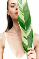 Elegant woman holding a large leaf, showcasing natural beauty and serenity in a bright, minimalist setting.